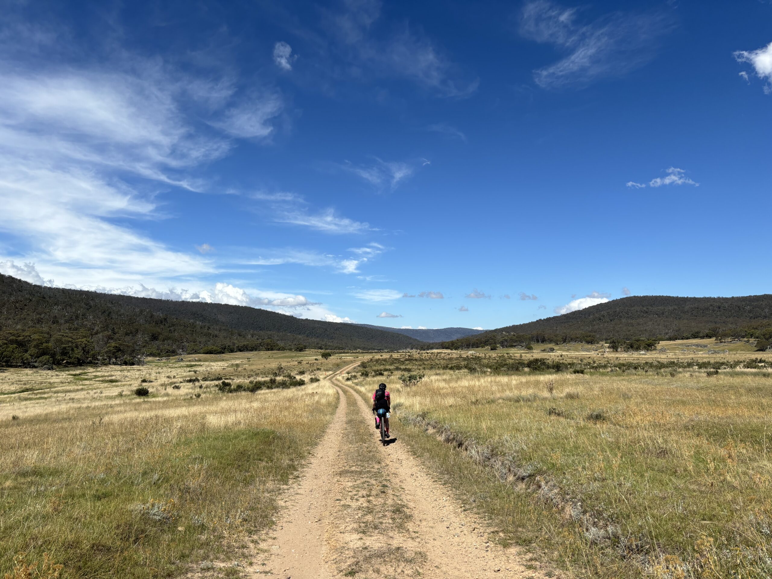 Solo cyclist riding long dirt road while reflecting on feeling behind in training